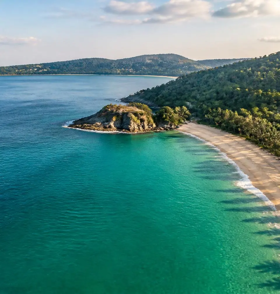 Aerial view of a quiet Phuket beach with turquoise water, headland and palm treeline