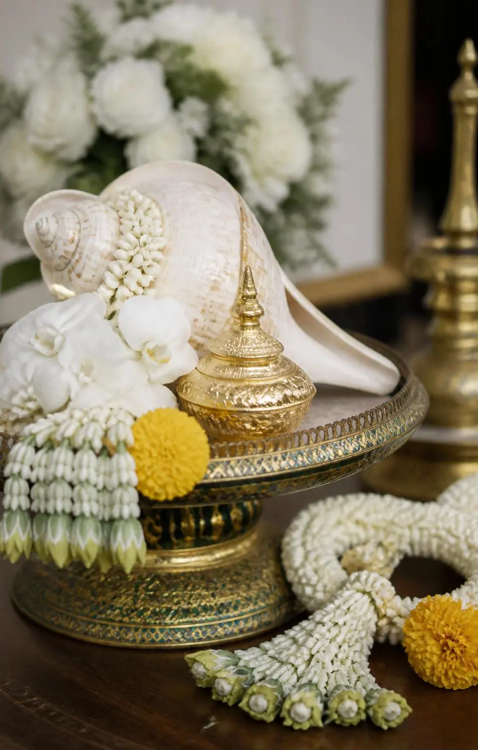 Thai wedding ceremony detail of marigold garlands, water shell and orchid blooms on a carved tray